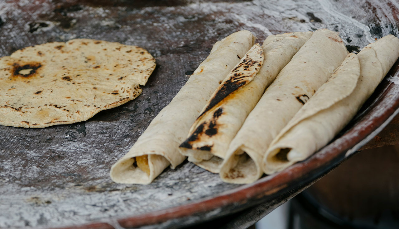 A close-up of several freshly made corn tortillas rolled and stacked on a wooden surface, showing authentic texture and slightly charred spots.