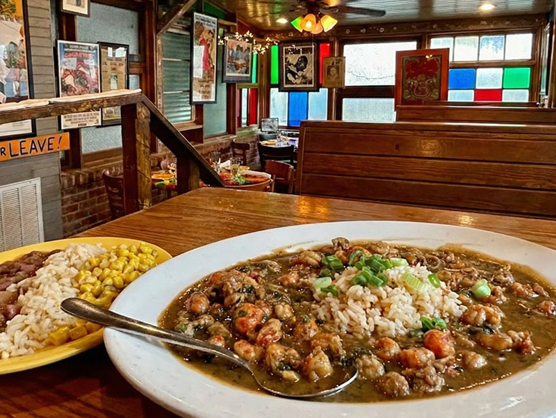 A plate of crawfish etouffee and a side of red beans and rice on a wooden table inside the eclectic interior of Jacques-Imo's Cafe in New Orleans.