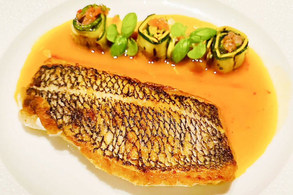 A gourmet seafood dish from Le Bernardin, featuring a perfectly seared piece of fish topped with a delicate herb garnish and served with a light sauce and sea beans.