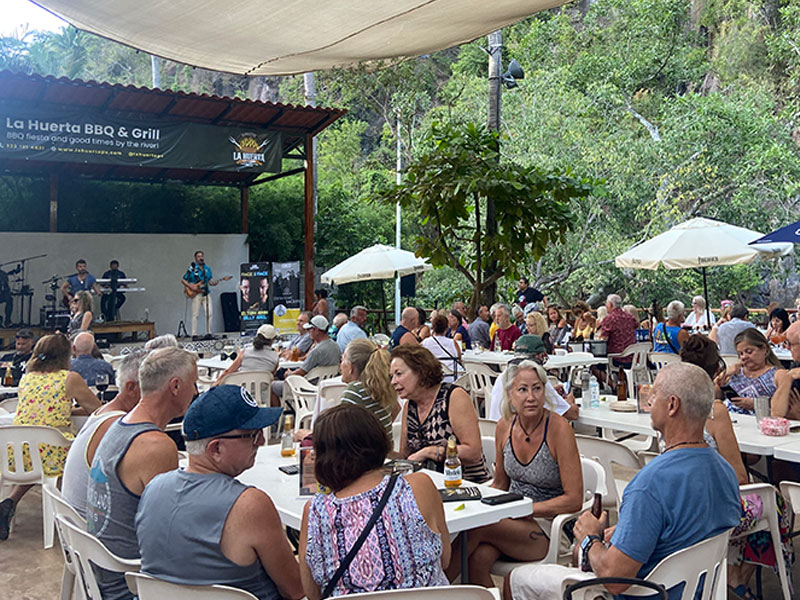 Wide shot of the outdoor dining area at La Huerta BBQ & Grill with many guests and live music.