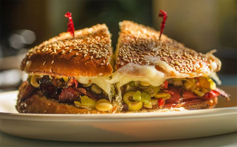 A close-up of a classic New Orleans Muffuletta sandwich from Napoleon House, featuring layers of Italian meats, melted provolone cheese, and thick olive salad on a seeded Sicilian loaf.