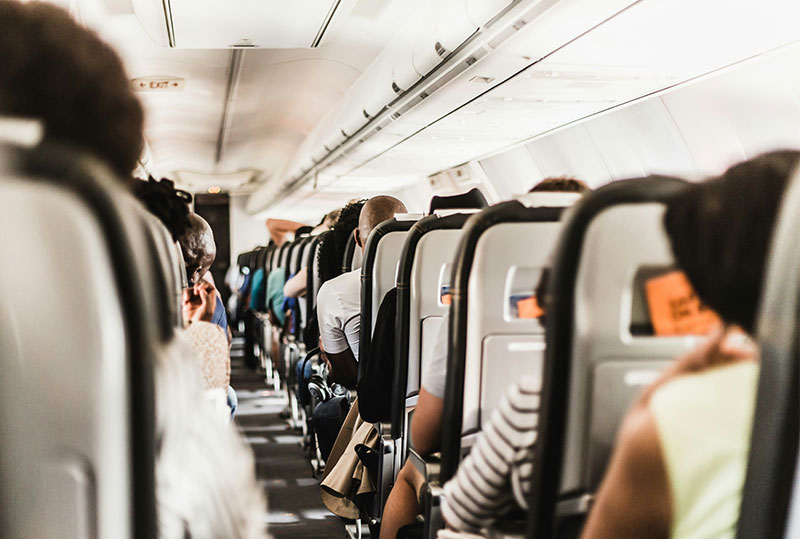 A view from the aisle of an airplane showing rows of passengers seated in a crowded cabin, with a focus on the narrow space and the back of the seats.