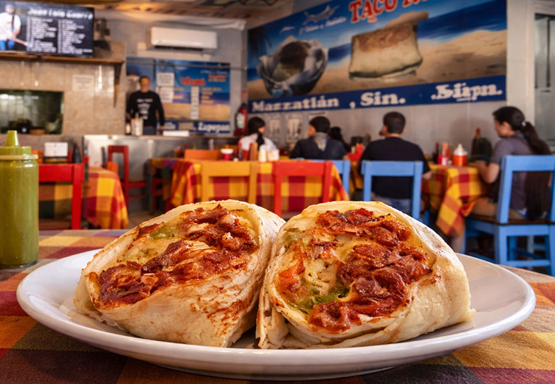 Interior of Tacón de Marlin in Puerto Vallarta with a close-up of a smoked marlin burrito on a table and colorful dining room in the background.