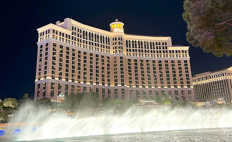 A stunning night view of the Bellagio Fountains in Las Vegas, with high-reaching water jets illuminated against the backdrop of the Bellagio Hotel and the dark desert sky.