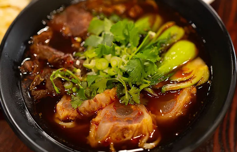 A colorful bowl of authentic Chinese beef noodle soup from the Chinatown Plaza in Las Vegas, garnished with fresh cilantro and bok choy.