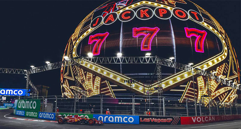 A vibrant night scene of the Formula 1 Las Vegas Grand Prix, showing race cars speeding past the bright neon lights and iconic casino facades of the Las Vegas Strip.