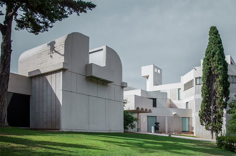 The modern white architecture of the Fundació Joan Miró museum on Montjuïc Hill in Barcelona, featuring bold primary-colored sculptures against a clear blue sky.