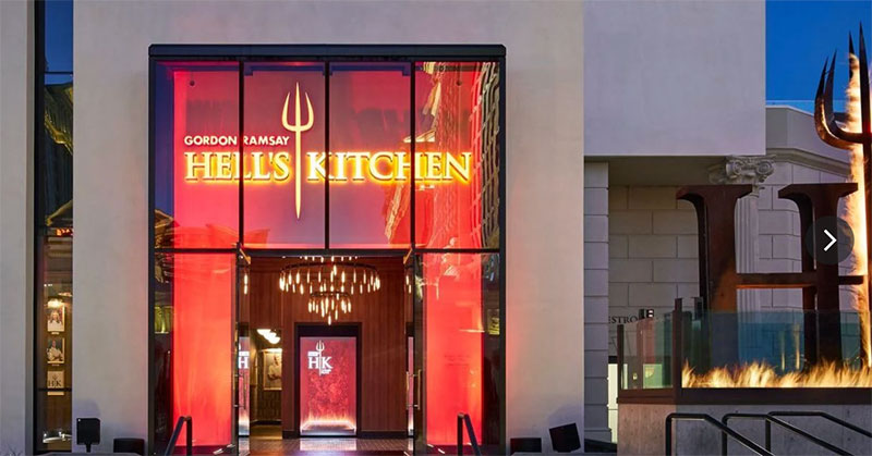 The exterior of Gordon Ramsay Hell's Kitchen at Caesars Palace, featuring the iconic pitchfork logo and glowing red neon signage against the evening sky