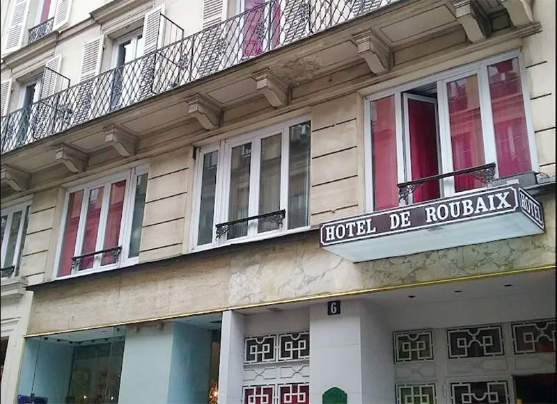 The classic painted red exterior sign of the Hôtel de Roubaix, located in a Haussmann-style building in the Le Marais neighborhood of Paris.