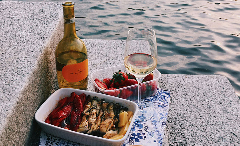 A traditional Italian meal of lasagna in a ceramic dish paired with two glasses of rosé wine on a table overlooking the water and mountains in Lake Como.