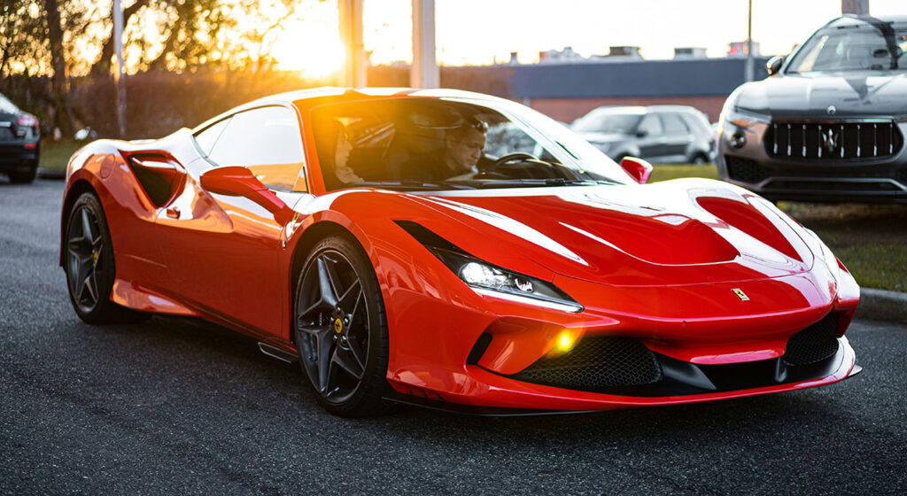 A red Ferrari F8 Tributo driving on a scenic road in Italy during sunset.