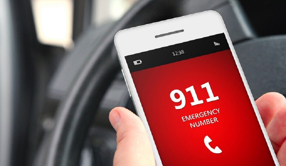A person holding a smartphone inside a car, displaying the emergency number 911 in large red digits on the screen.
