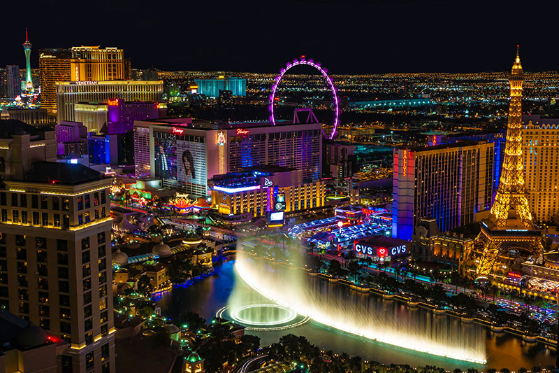 Alt Text: A vibrant night view of the Las Vegas Strip, featuring the illuminated High Roller observation wheel, glowing neon signs from various resorts and casinos, and the bright lights of city traffic under a dark sky.