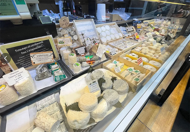 A close-up view of a vibrant cheese stall inside the Marché des Enfants Rouges, featuring diverse wheels and wedges of French cheese arranged on tiered displays.