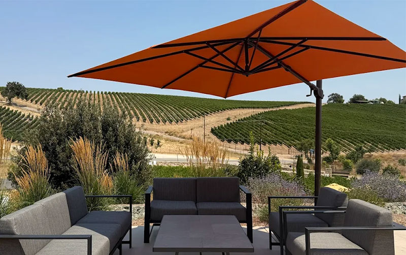 sun-drenched A outdoor patio at McPrice Myers Wines in Paso Robles, featuring black mesh tables under large orange umbrellas with a scenic view of rolling vineyard hills in the background.