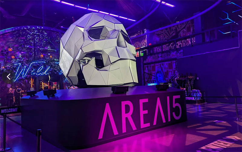 A wide view of the entrance to Omega Mart at AREA15 in Las Vegas, featuring the "AREA15" neon sign and the surreal, glitchy grocery store storefront under vibrant purple and blue lights.