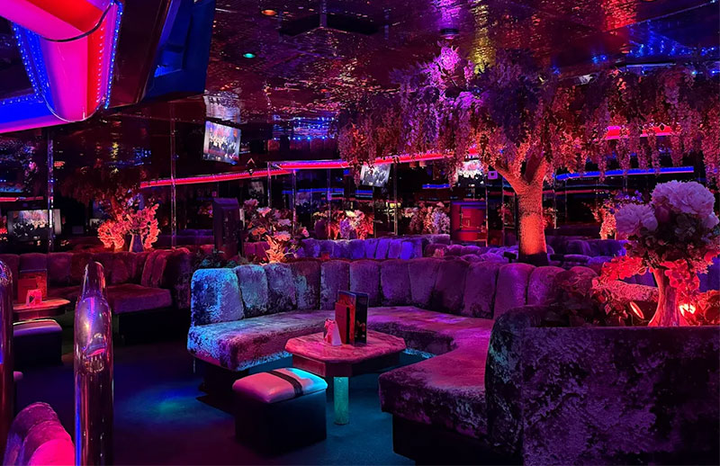 The interior of the Peppermill Fireside Lounge, featuring plush purple velvet booths, neon pink and blue lighting, and a central fire pit reflecting on the water.