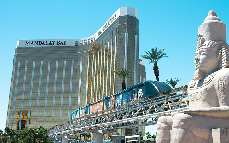 A daytime view of the golden Mandalay Bay hotel towers in Las Vegas, showcasing the resort's iconic architecture against a bright blue sky