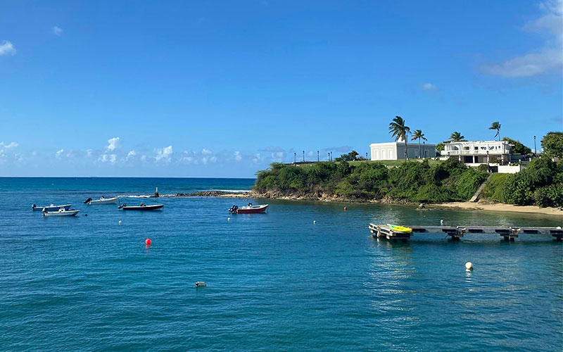 View of the lush coastline and a historic white lighthouse on the island of Vieques from the deck of an arriving ferry.