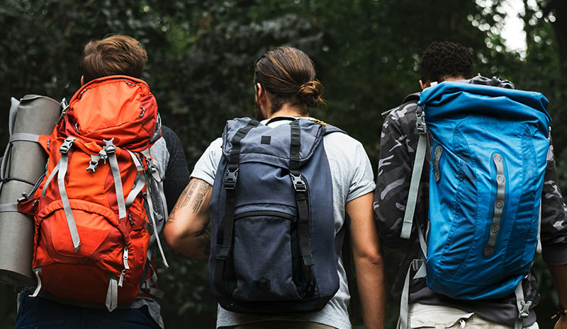 Three pilgrims with large backpacks walking on the trail toward a village.
