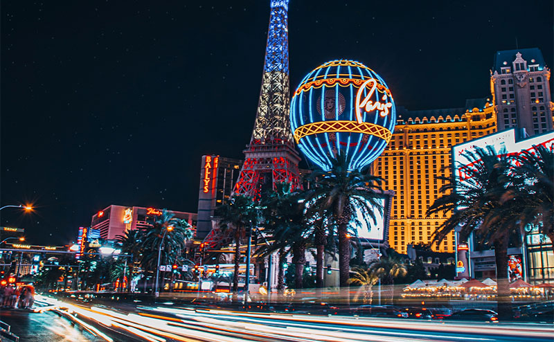 A night view of the Las Vegas Strip during the F1 Grand Prix, featuring the illuminated Eiffel Tower at Paris Las Vegas and the High Roller observation wheel in the background.