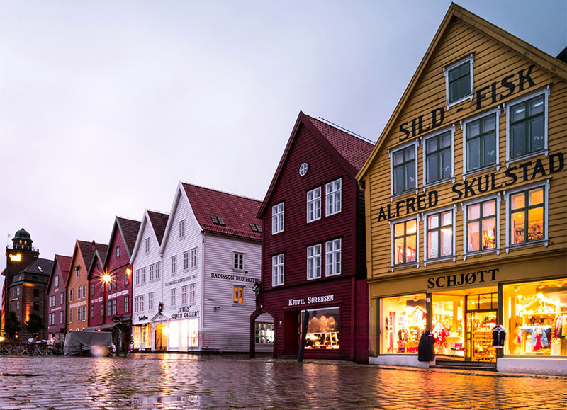 The colorful historic wooden houses of Bryggen Hanseatic Wharf in Bergen, Norway, illuminated at twilight.
