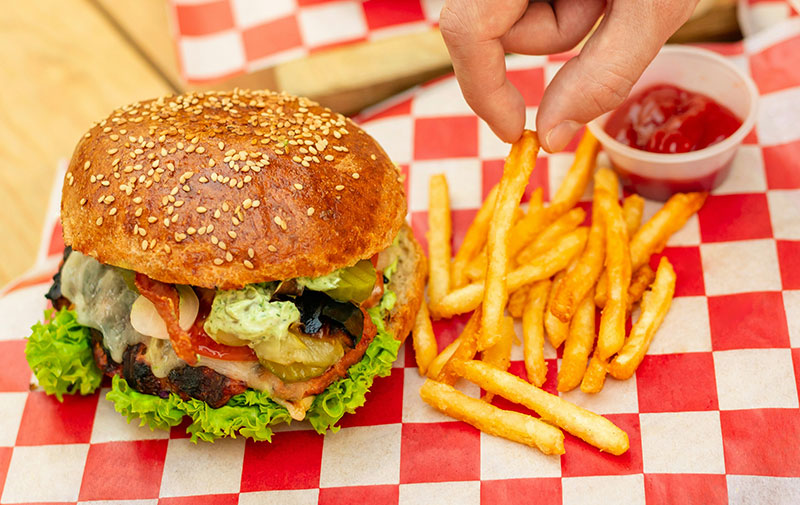 A close-up of a classic American cheeseburger with lettuce and tomato on a sesame seed bun, served with a side of crispy golden french fries on a red and white checkered paper liner.