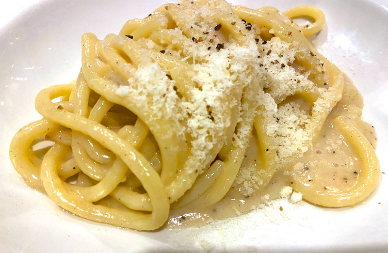 Plate of cacio e pepe pasta topped with grated cheese and black pepper in Rome