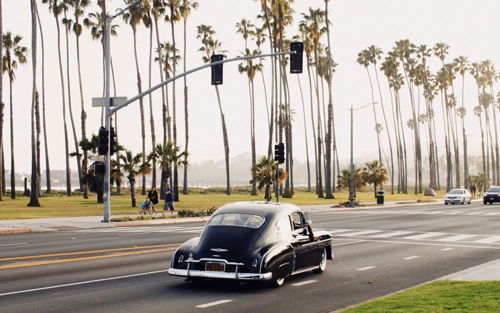 Vintage black car driving down the palm-lined Cabrillo Boulevard in Santa Barbara.