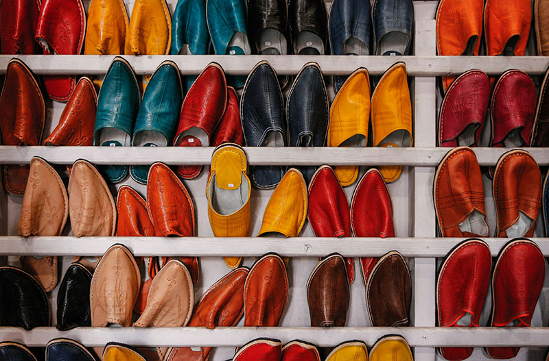 Rows of brightly colored traditional Moroccan leather slippers called babouches displayed on wooden shelves.