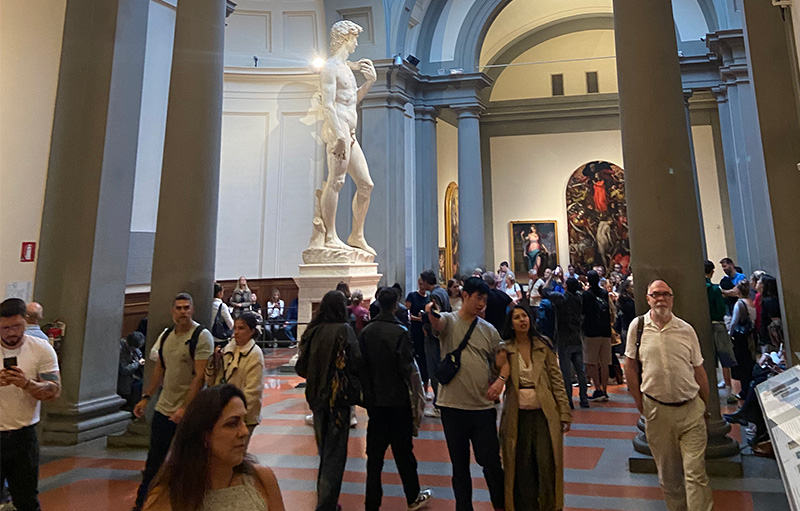 Visitors inside a Florence museum hall with Michelangelo’s David statue under a skylit dome