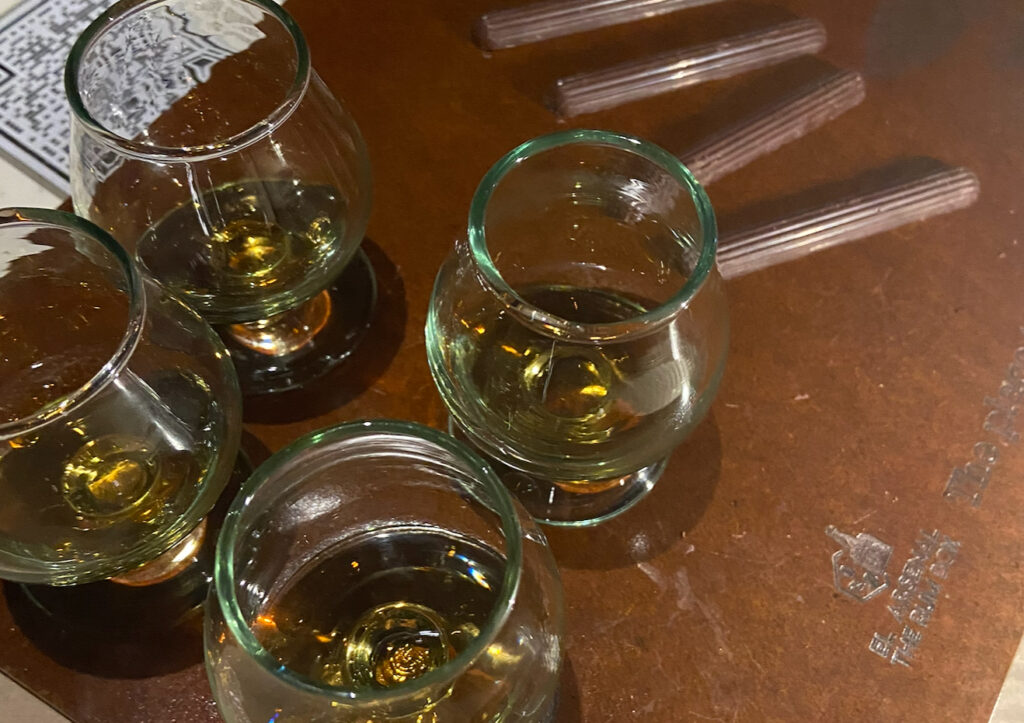 Four glass snifters filled with Colombian rum alongside sticks of local chocolate on a wooden tasting board at El Arsenal The Rum Box