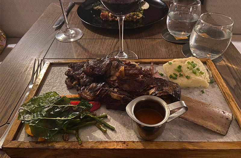 Large bone-in beef rib served on a stone platter with side dishes and a glass of red wine at El Burlador Gastrobar