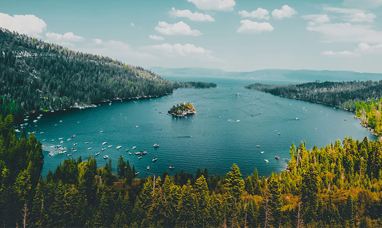 High angle view of boats gathered in the vivid blue waters of Emerald Bay at Lake Tahoe surrounded by dense pine forests.