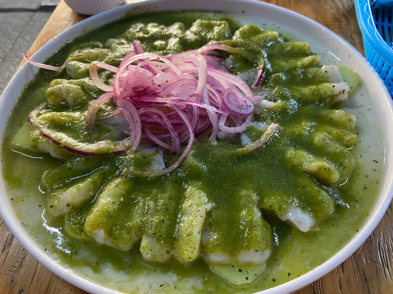 Plate of fresh shrimp aguachile covered in green salsa and sliced red onions.