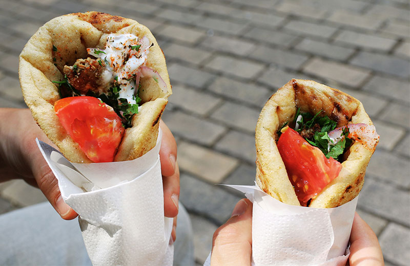 Alt Text: A close-up of two authentic Greek gyros wrapped in warm pita bread, stuffed with seasoned rotisserie meat, fresh tomato slices, red onions, and crispy fries.