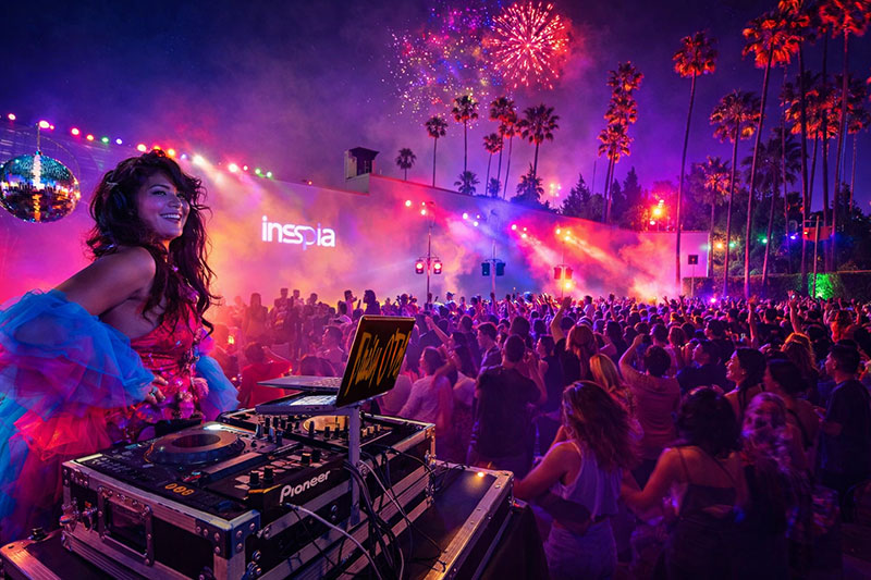 DJ performing at the Cinespia Hollywood Forever Cemetery movie night after-party with colorful stage lights and a crowd dancing under palm trees.