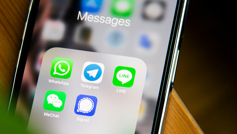 A close-up of an iPhone screen showing the WhatsApp app icon among other messaging folders, held by a traveler in a French setting.