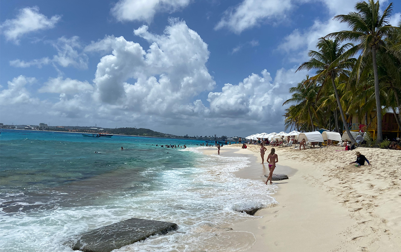Johnny Cay beach with people walking and white umbrellas.