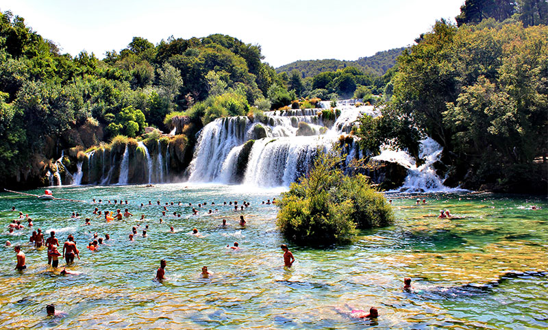 Tourists swimming in the turquoise water below the wide Skradinski Buk waterfall in Krka National Park, Croatia.