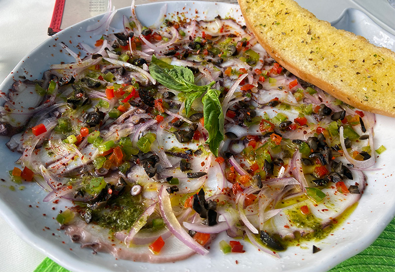 A plate of thinly sliced octopus carpaccio topped with peppers and olives served with garlic bread at La Regatta restaurant in San Andres.