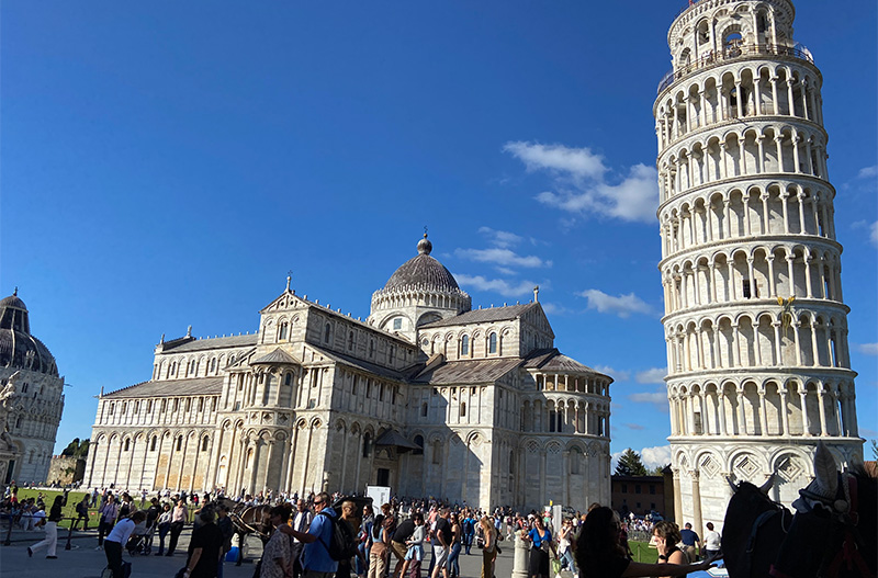 The Leaning Tower of Pisa beside the Pisa Cathedral under a bright blue sky