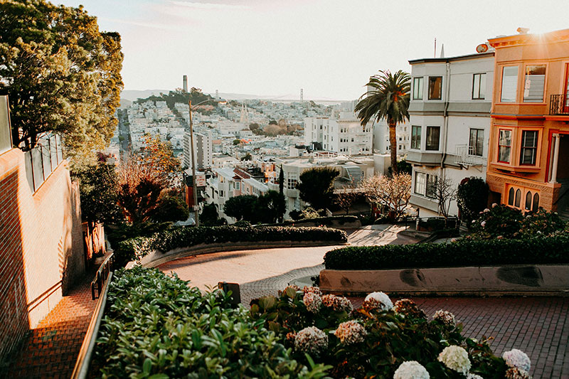 View down the brick-paved, winding curves of Lombard Street in San Francisco bordered by houses and gardens at golden hour