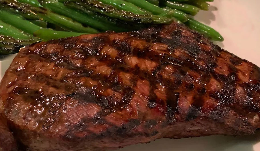 A large, char-grilled steak served with a side of green beans and a packet of butter on a white plate at Mancini's.
