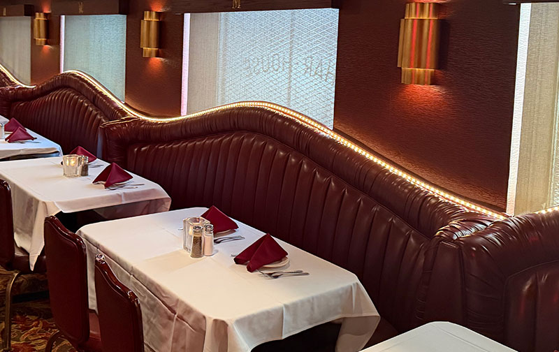 Classic, retro red leather semi-circular booths set with white tablecloths and burgundy napkins in the dining room of Mancini's Char House.