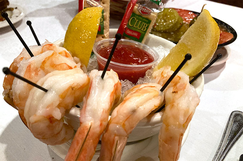 A classic shrimp cocktail appetizer served over ice with lemon wedges, cocktail sauce, and crackers at Mancini's Char House.