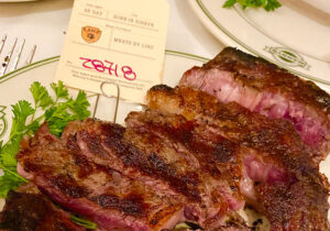 Sliced 85-day dry-aged bone-in ribeye steak on a plate with a meat tag at Manny's Steakhouse