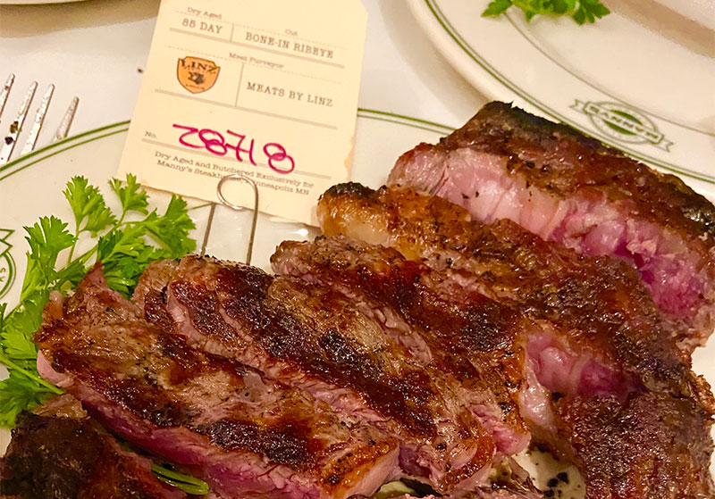 Sliced 85-day dry-aged bone-in ribeye steak on a plate with a meat tag at Manny's Steakhouse