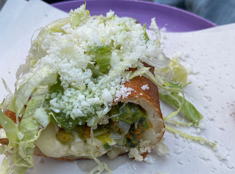 lose up of a Mexican torta sandwich with meat and green salsa being held by a hand.