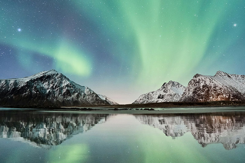 Vibrant green Aurora Borealis dancing in the night sky over Skagsanden Beach in the Lofoten Islands, Norway.